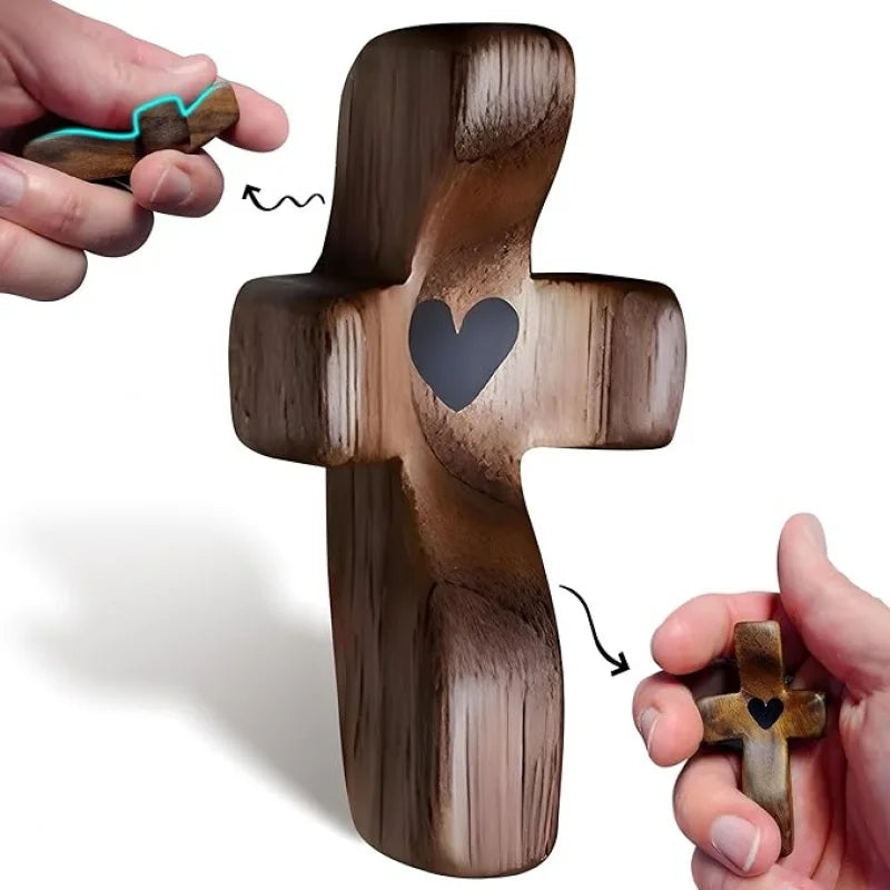A dark brown wooden comfort prayer cross with a carved heart detail, shown being held by a hand.