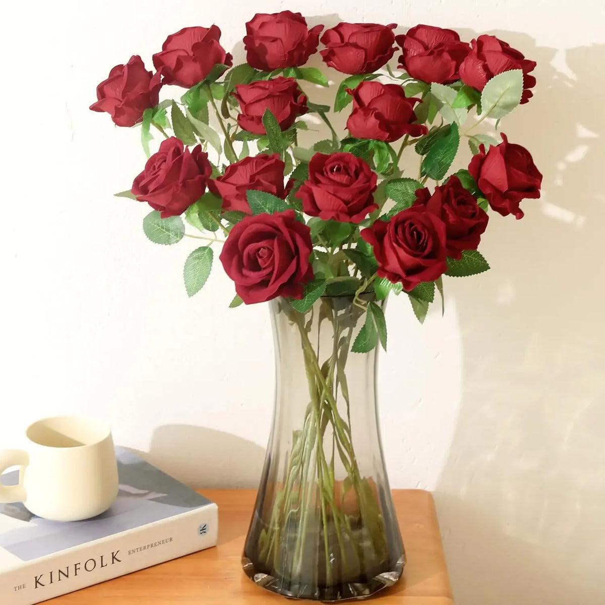 A bouquet of deep red velvet artificial roses in a clear glass vase on a wooden surface.