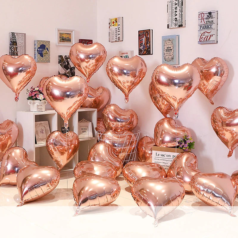 A collection of gold heart foil balloons displayed against a white wall and shelving unit.