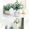 A glass vase filled with green eucalyptus leaves displayed on a white marble surface.