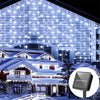 Solar LED icicle string lights illuminating a snowy house facade at night