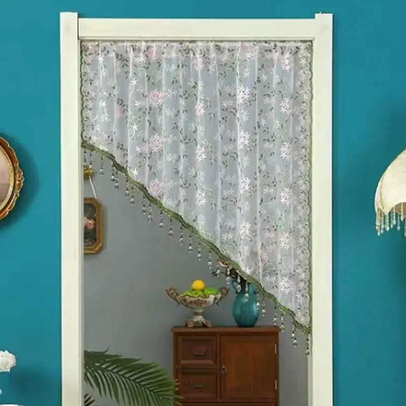 A sheer floral lace curtain hangs in a white frame against a teal wall.