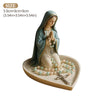 A statue of the Virgin Mary with a green mantle and a rosary holder on a light-colored tray