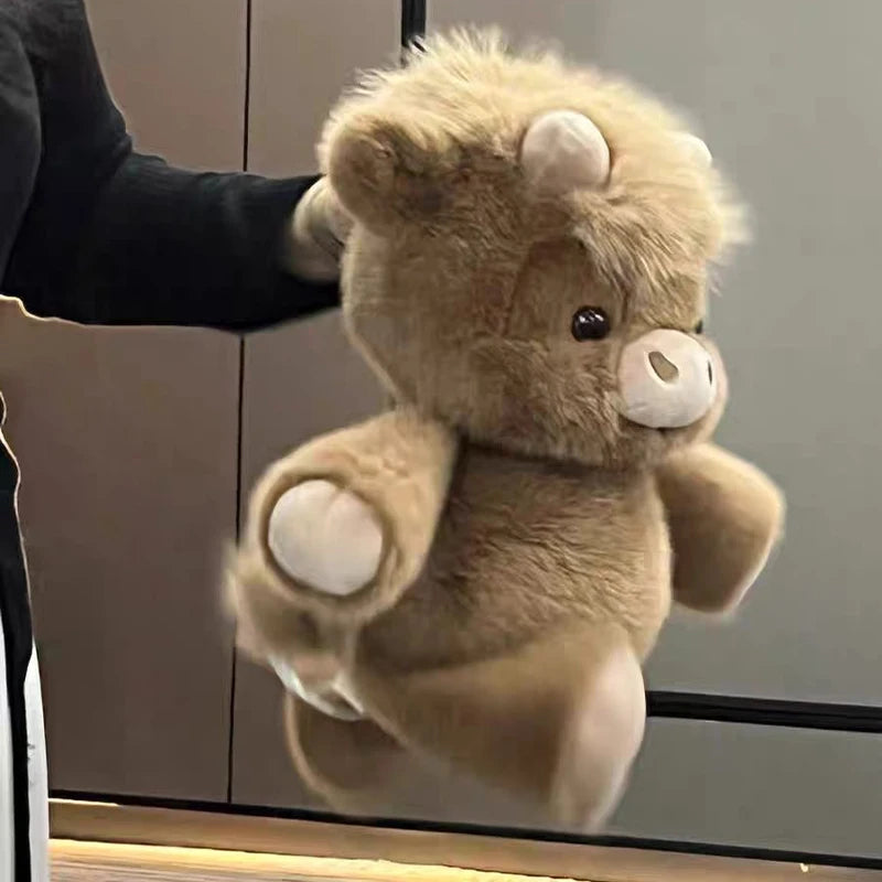 Un jouet en peluche de veau écossais brun et duveteux est tenu par une personne sur un fond sombre.