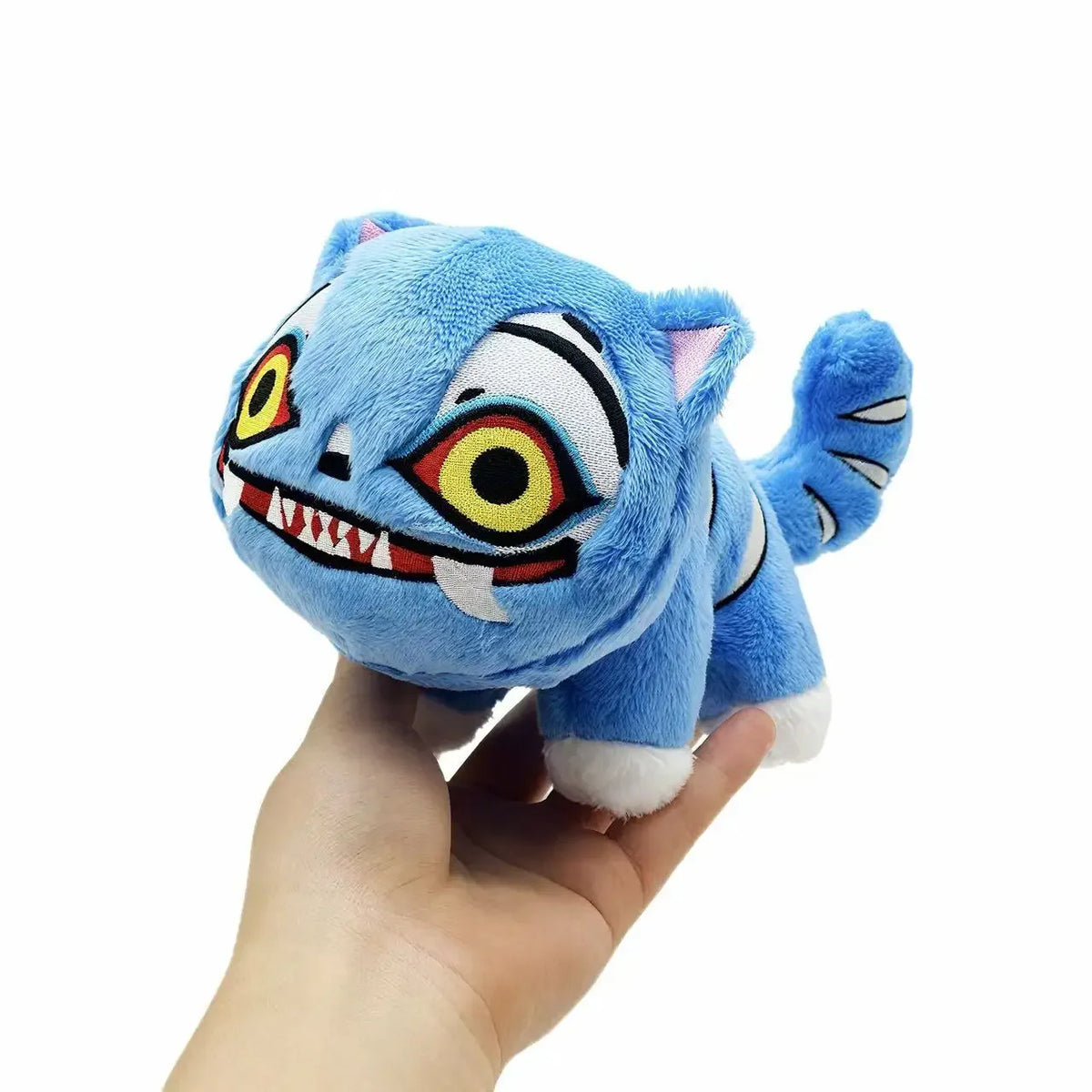A hand is holding a blue tiger plush toy with white and black stripes and large yellow eyes.