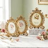 Vintage gold oval resin picture frame displayed on a marble surface with roses and greenery.