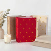 A red photo album with gold foil hearts sits next to two neutral-colored albums on a white surface.