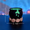 A black resin miniature ghost decor with a green liquid dripping from the top, resting on a light brown base.