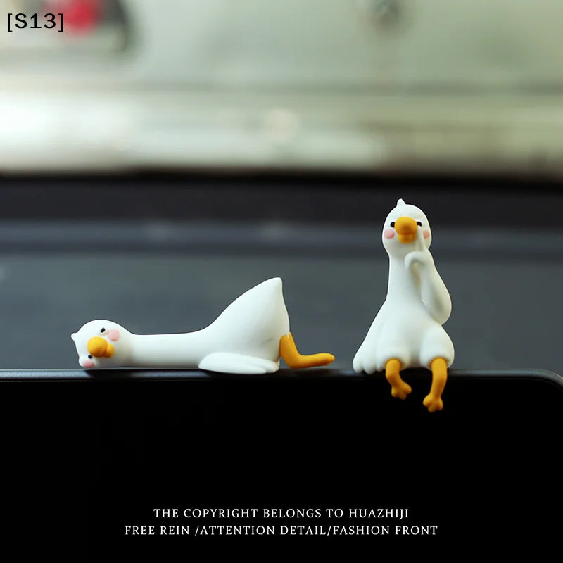 A white resin cartoon duck figurine with yellow feet sitting on a black surface.