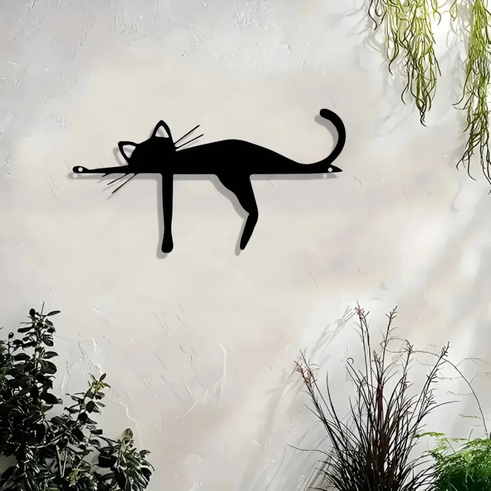 A black silhouette of a cat sculpture mounted on a white wall with green foliage in the background.