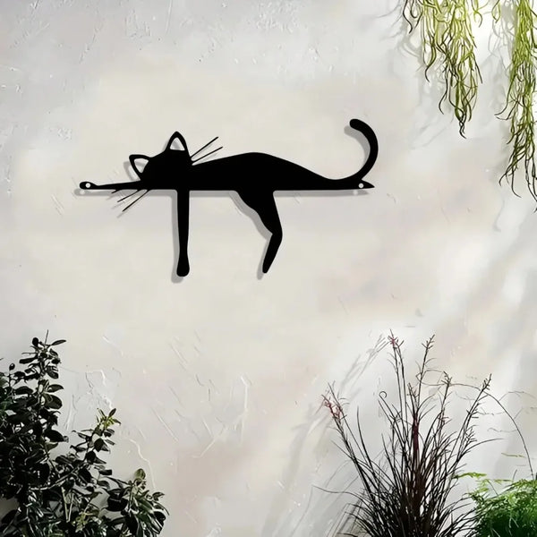 A black silhouette of a cat sculpture mounted on a white wall with green foliage in the background.