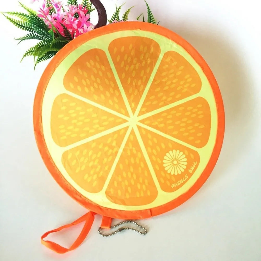 Round orange fruit design foldable hand fan with green foliage in the background