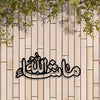 Islamic calligraphy metal wall art featuring the Arabic phrase Ma'a Allah on a light wood panel with green foliage above.