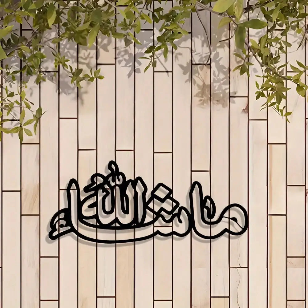 Islamic calligraphy metal wall art featuring the Arabic phrase Ma'a Allah on a light wood panel with green foliage above.