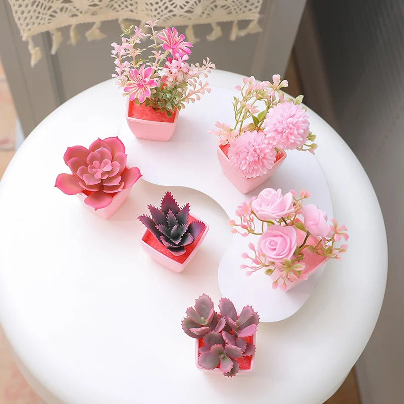 A set of six artificial potted plants in various shades of pink and purple arranged on a white surface.
