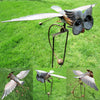 A metal wind spinner garden decoration featuring a bird-like figure with wings and a long metal rod.