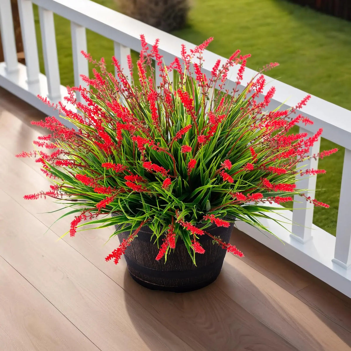A potted artificial lavender plant with bright red flowers sits on a wooden deck railing.