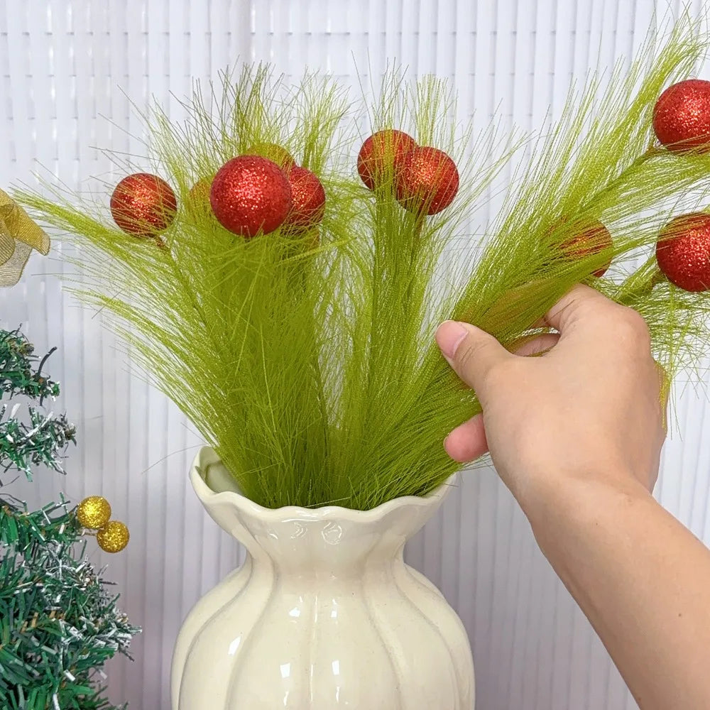 A hand is arranging Christmas tree decor picks featuring bright green grass and red berries in a white vase.