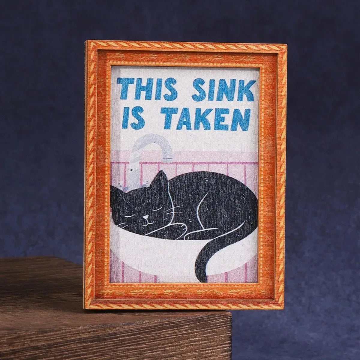 Impresión enmarcada de un gato negro durmiendo sobre fondo rosa con el texto 'Este lavabo está tomado'.