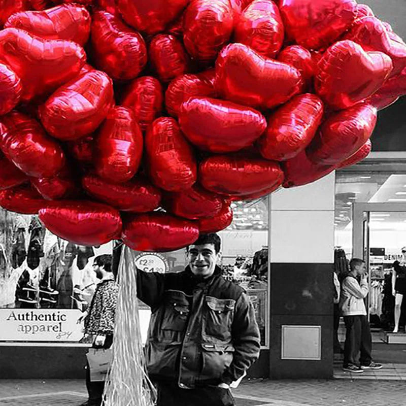 A close-up shot of a large cluster of red heart-shaped foil balloons.