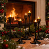A set of black minimalist candle holders with yellow flames arranged on a wooden surface near a fireplace.