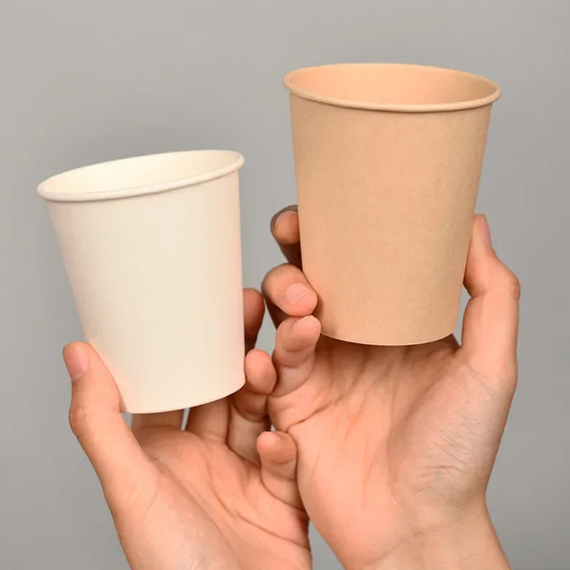 A person is holding a light brown disposable paper cup against a gray background.