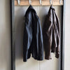 Two dark leather coats are hanging on wooden wall hooks.