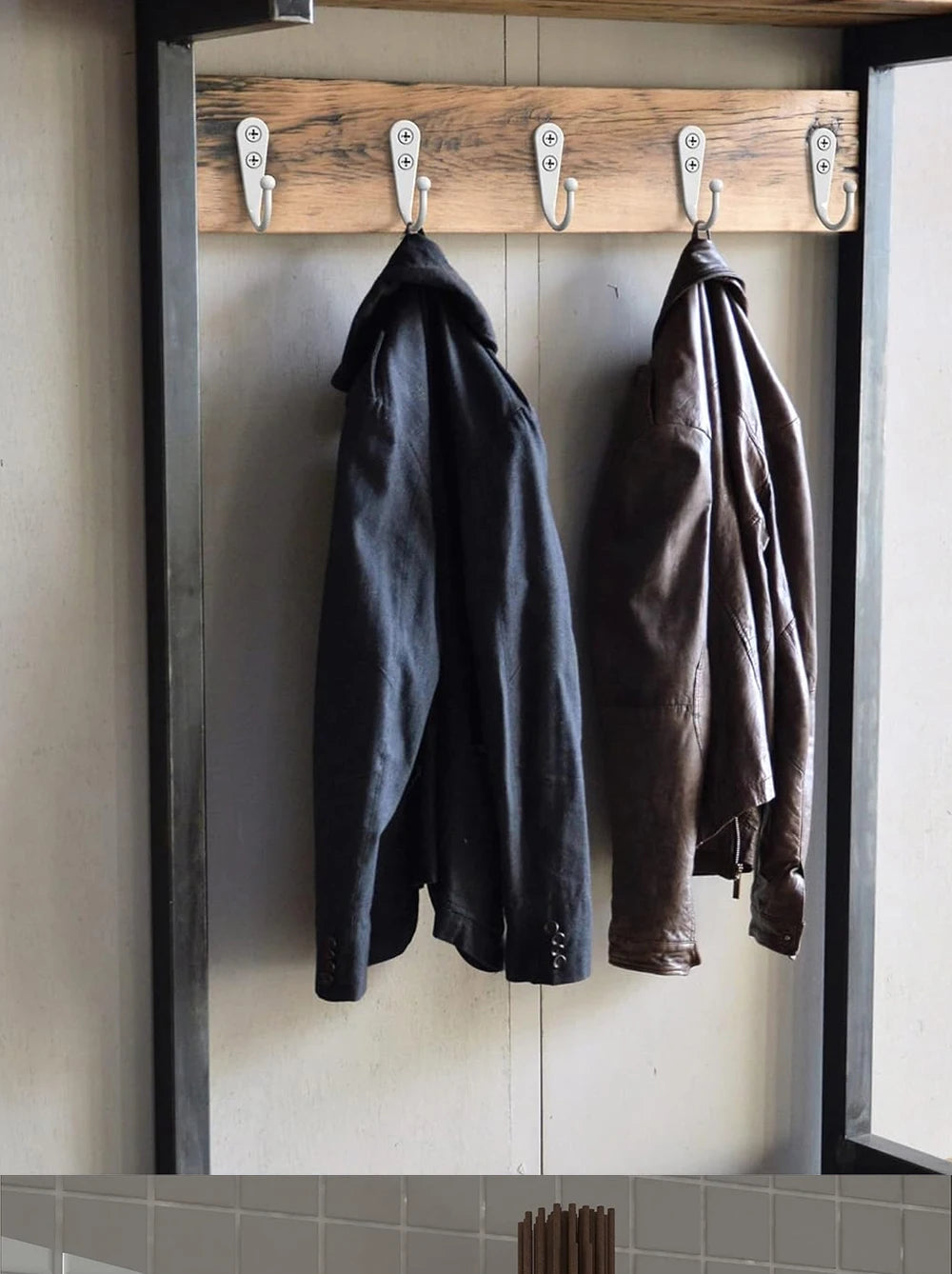Two dark leather coats are hanging on wooden wall hooks.