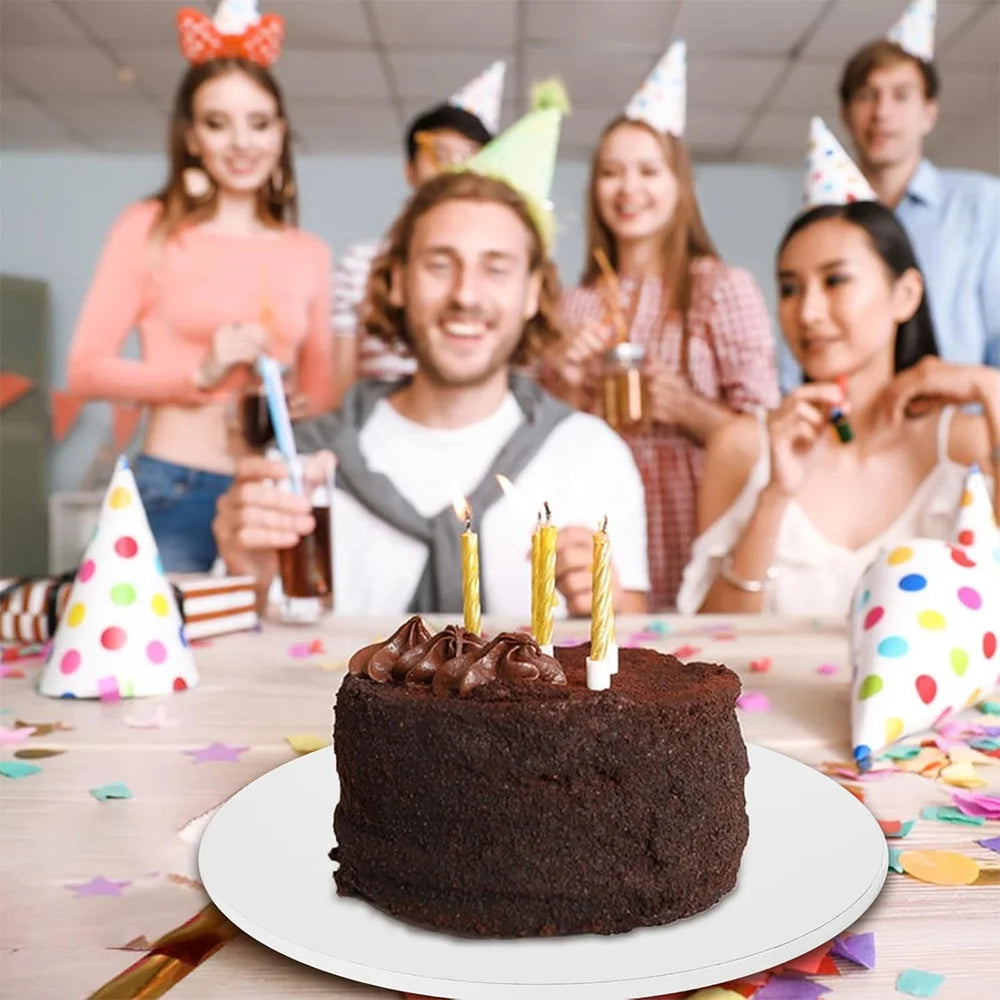 A dark chocolate round cake decorated with frosting and lit candles on a white plate.