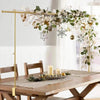 A gold adjustable balloon arch stand with greenery and white floral garlands decorating a wooden table.