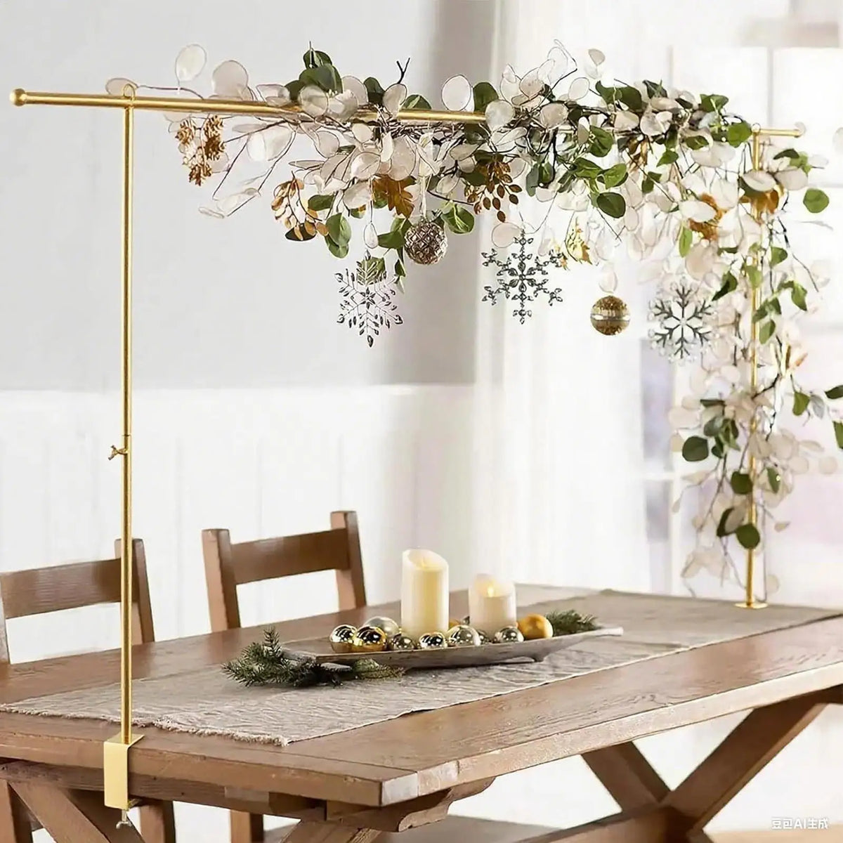 A gold adjustable balloon arch stand with greenery and white floral garlands decorating a wooden table.