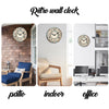 A rustic wooden wall clock with Roman numerals hangs on a white wall in an indoor setting.