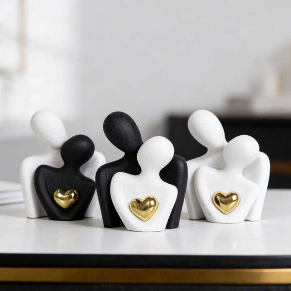A set of three abstract ceramic sculptures depicting a couple hugging, in black and white with gold heart accents.