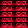 Set fluoreszierender herzförmiger LED-Partybrillen in Rasterform vor dunkelrotem Hintergrund