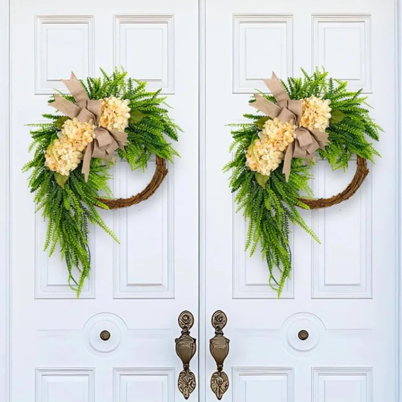 A rustic green hydrangea wreath with a burlap bow hangs on a white door.