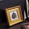 A gold-framed picture featuring a black silhouette of a sleeping bear, displayed on a dark surface.