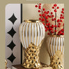 A golden ceramic decorative vase with white stripes holds red berries and branches on a light background.
