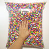 A hand is reaching into a clear bag filled with colorful pastel foam beads for crafting and decoration.