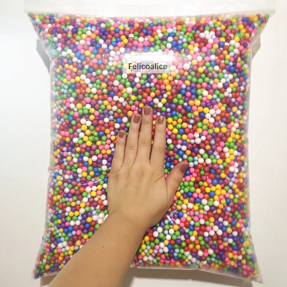 A hand is reaching into a clear bag filled with colorful pastel foam beads for crafting and decoration.