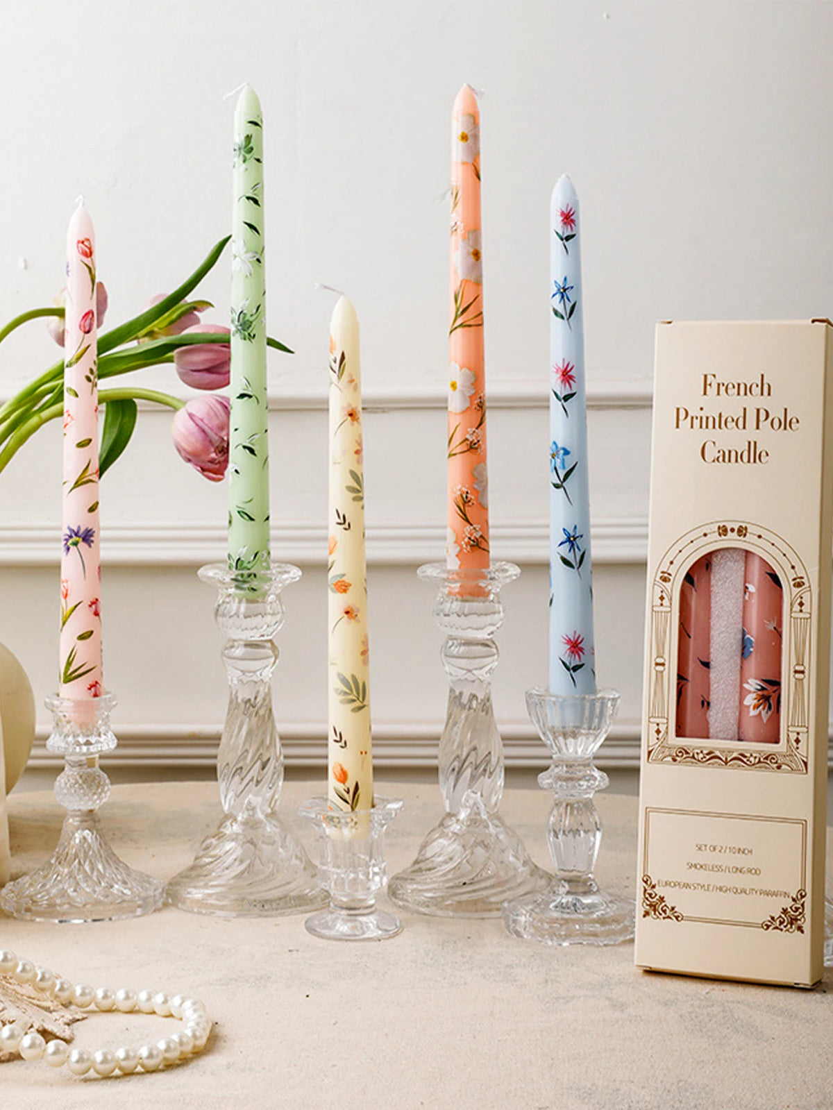 A collection of decorative printed long stick candles in pink, green, and blue are displayed on a light surface.