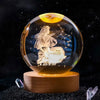 A crystal ball with a golden orb and an engraved image of a praying figure against a starry background.