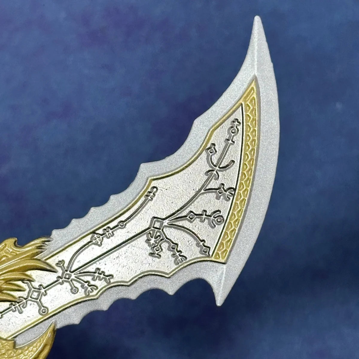 A close-up of a collectible miniature sword featuring intricate etched patterns and a silver blade with gold accents.