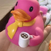 A pink rubber duck bath toy with a yellow accessory is held in a hand.