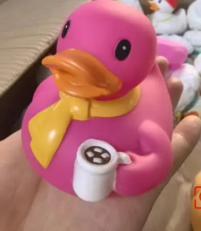 A pink rubber duck bath toy with a yellow accessory is held in a hand.