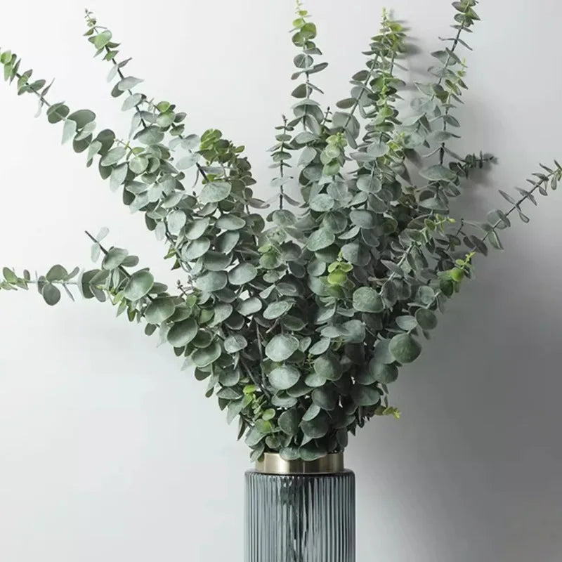 A bouquet of artificial eucalyptus stems with silvery-green leaves displayed in a glass vase.
