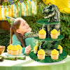 A 3-tier dinosaur cupcake stand decorated with green foliage and yellow cupcakes for a party.