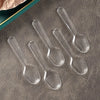 A collection of clear plastic disposable spoons arranged on a gray surface.