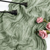 A light blue cheesecloth table runner draped in soft folds with dark metal utensils and pink roses.
