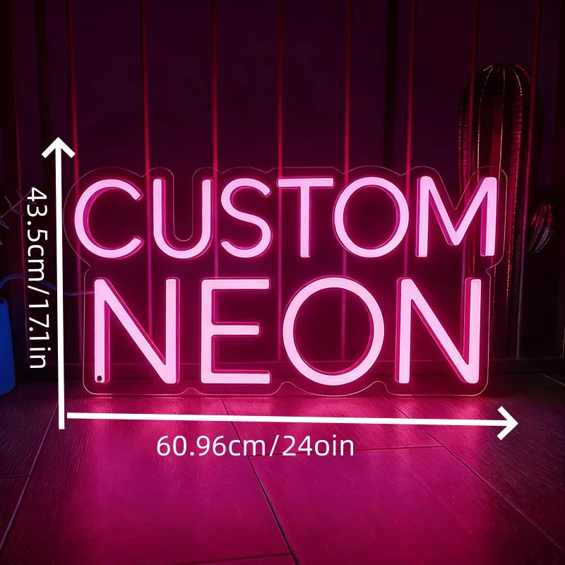 A glowing pink neon sign spelling CUSTOM NEON is displayed on a dark surface.