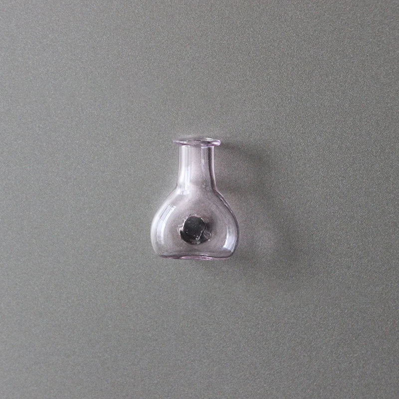 A clear glass bottle or vial with a narrow neck is mounted on a gray wall.